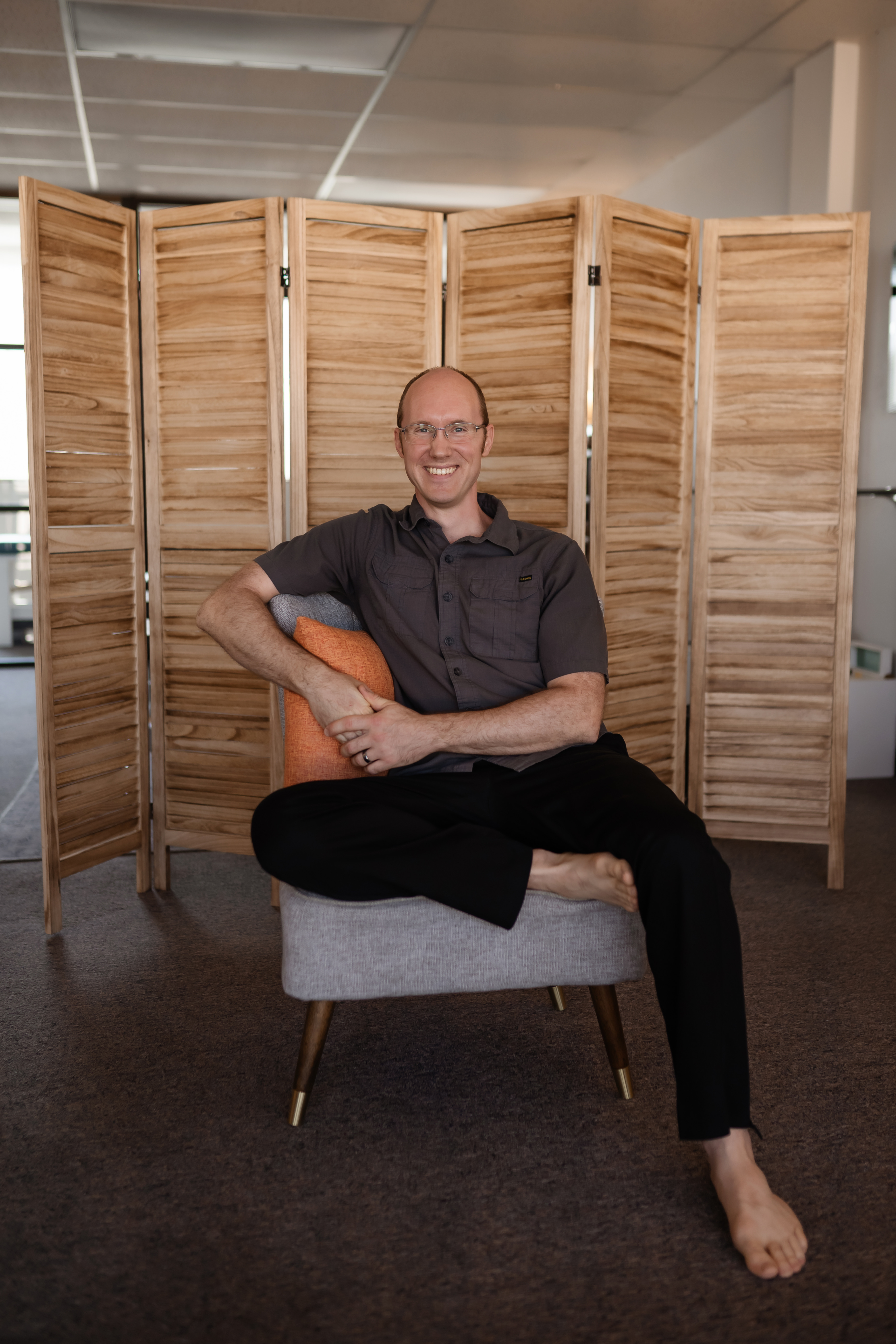 Jason Dixon seated in a grey chair in front of a wooden folding screen, smiling